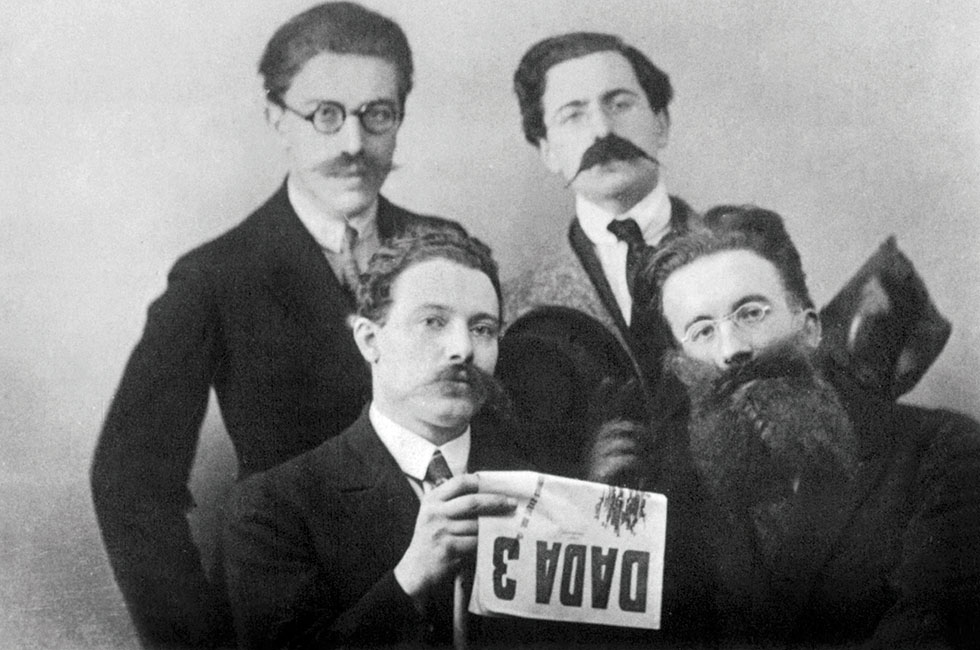 Les ecrivains Dada : derriere : Andre Breton, Rene Hilsum ; devant : Louis Aragon et Paul Eluard deguises lisant la revue Dada 3, 1919 --- Dadaist writers : top : Andre Breton, Rene Hilsum ; bottom : Louis Aragon and Paul Eluard, costumed, reading Dada 3, 1919